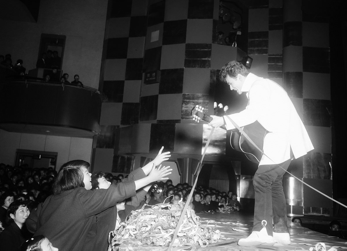 Micky Curtis, an Elvis Presley-style singer, strums his guitar and sings just beyond reach of female admirers in the Nichigeki Theater in Tokyo on February 18, 1958.