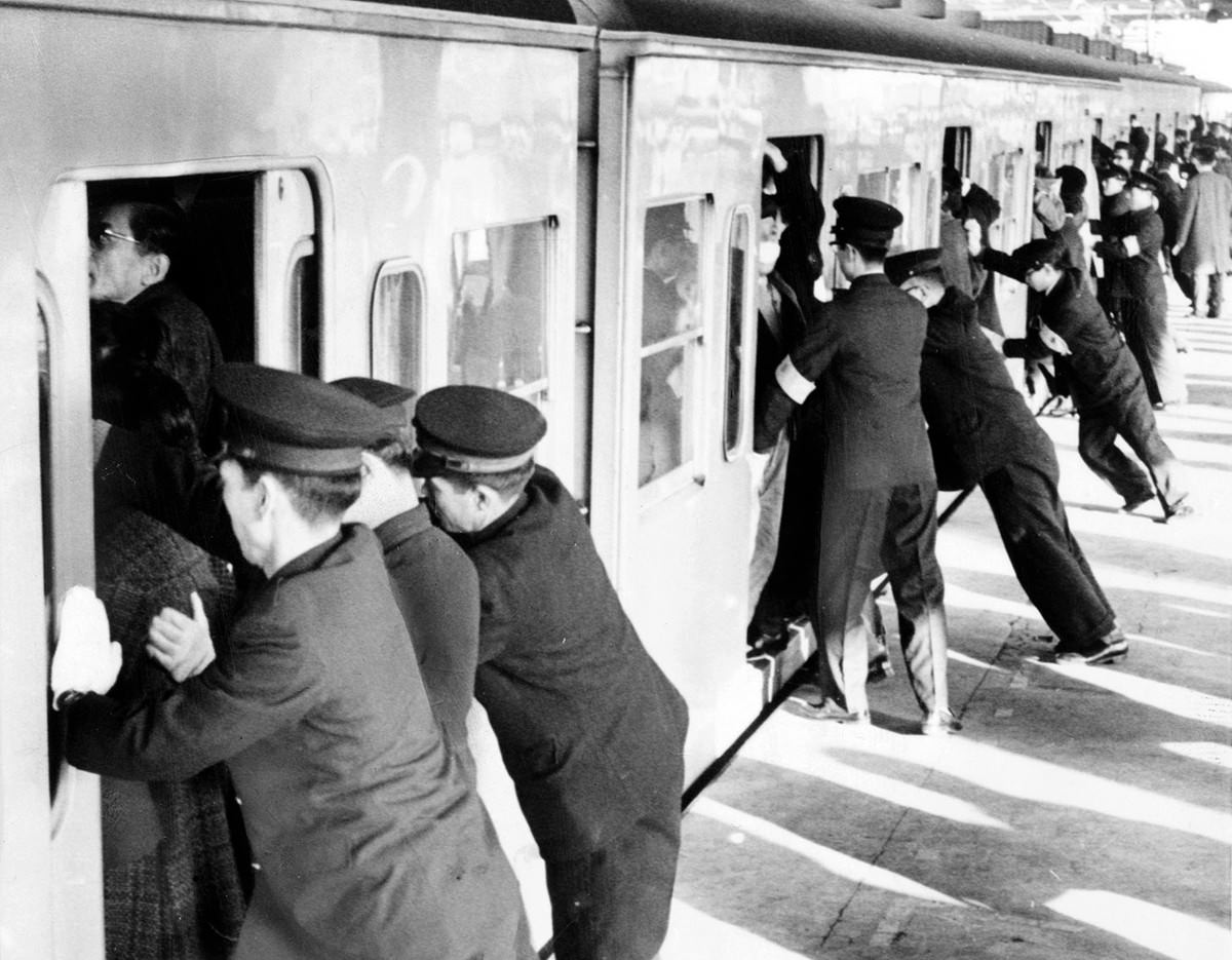 College students employed as uniformed "pushers" cram commuters into railroad passenger cars in Tokyo.