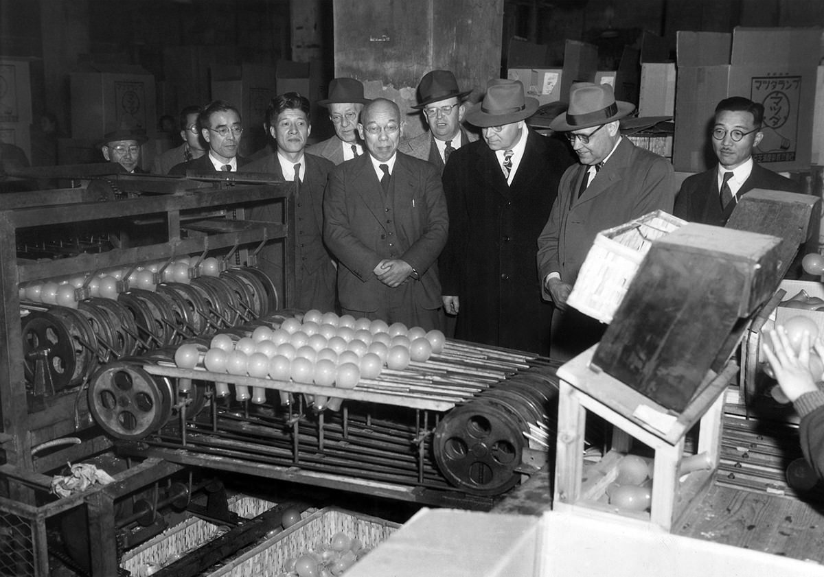 Industrial training experts watch a light bulb machine drop bulbs down to other workers who sort them according to defects at Tokyo Shibaura Electric Co. in Tokyo on January 25, 1951.