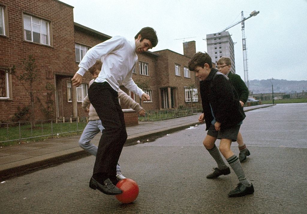Manchester United footballer George Best playing football in the street with some local boys near his family's home in Belfast, Northern Ireland, circa 1967.