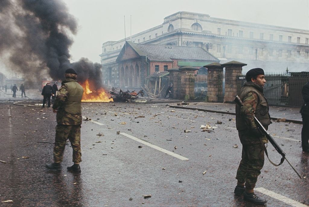 British Army soldiers standing guard as firemen deal with a fire on a street during a period of rioting in Belfast, Northern Ireland on 14th August 1969.