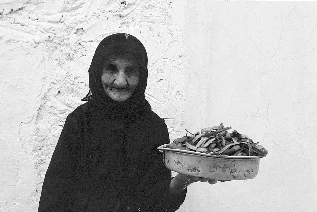 An old woman with a pot full of pods. Greece, 1970s.