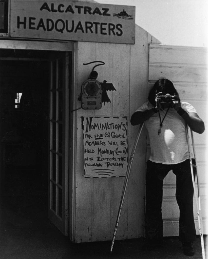 A Native American man on crutches takes a picture during a takeover of Alcatraz Island by a group of Native Americans, San Francisco, June 1970.