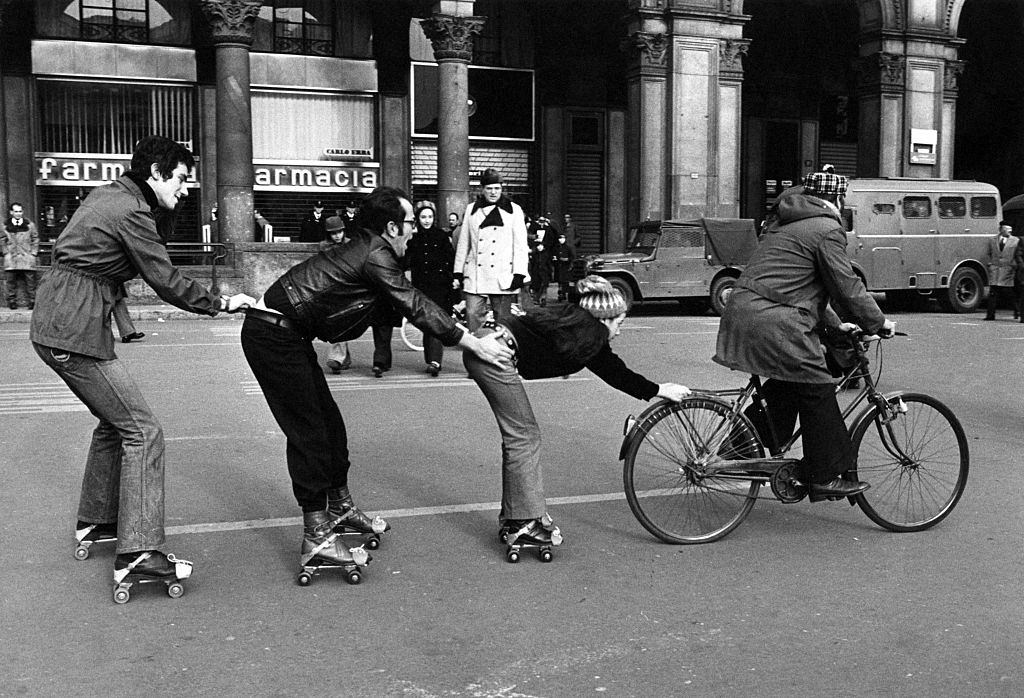 A man in bicycle drawing a little girl and two boys in roller skates on Piazza del Duomo during the first Italian walking sunday due to the oil crisis, 1973.