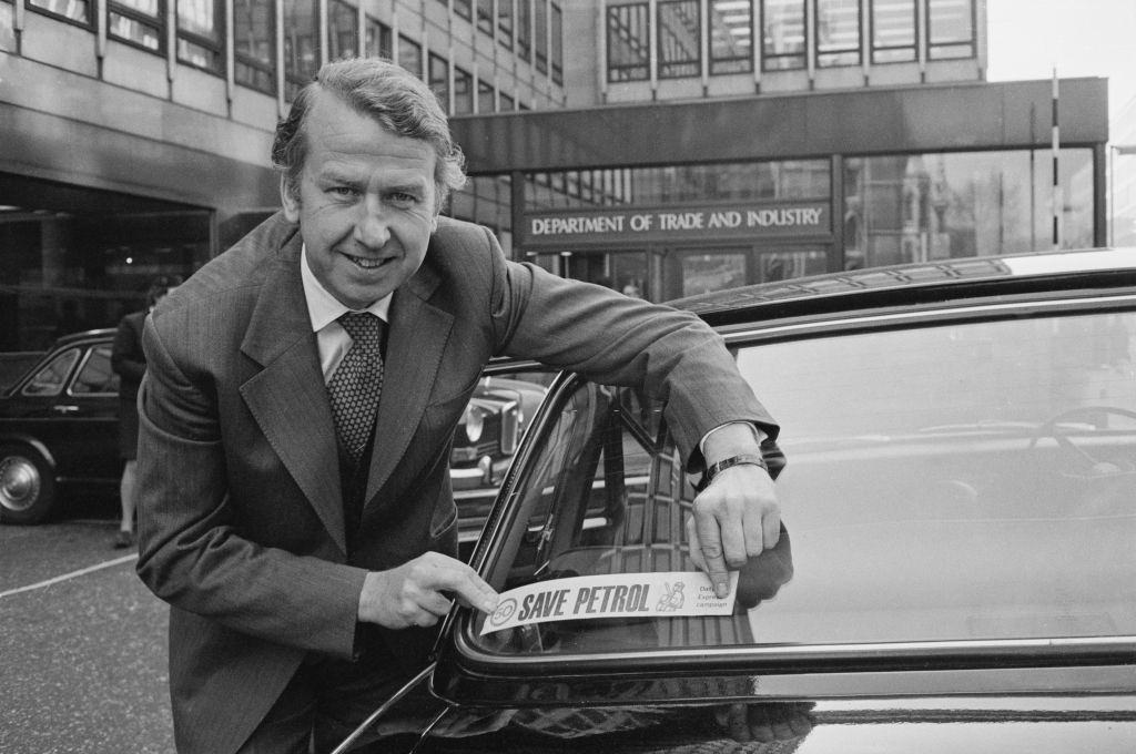 British Conservative Party politician, Peter Walker attaching a 'Save Petrol' sticker to the rear window of a car, London, November 1973.