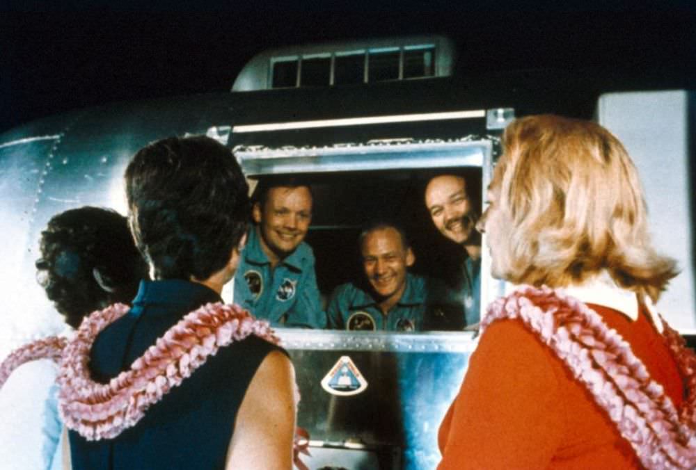 Astronauts Neil Armstrong, Buzz Aldrin, and Michael Collins greet their wives from the Mobile Quarantine Facility aboard the U.S.S.