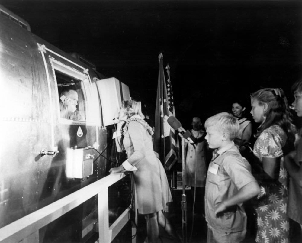 Joan Aldrin speaks on the phone to her husband, Buzz, while he gazes out from the Apollo 11 Mobile Quarantine Facility aboard the U.S.S.