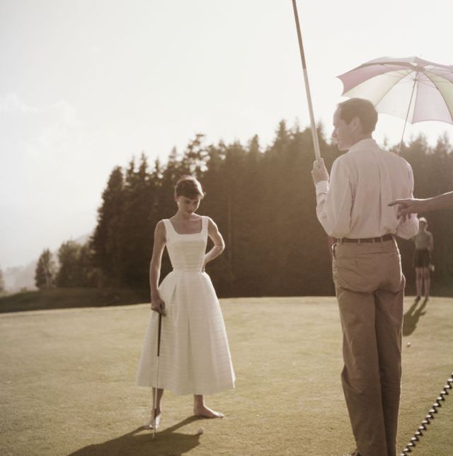 Audrey Hepburn standing on the golf course at Switzerland's Bürgenstock resort near husband Mel Ferrer, 1954.