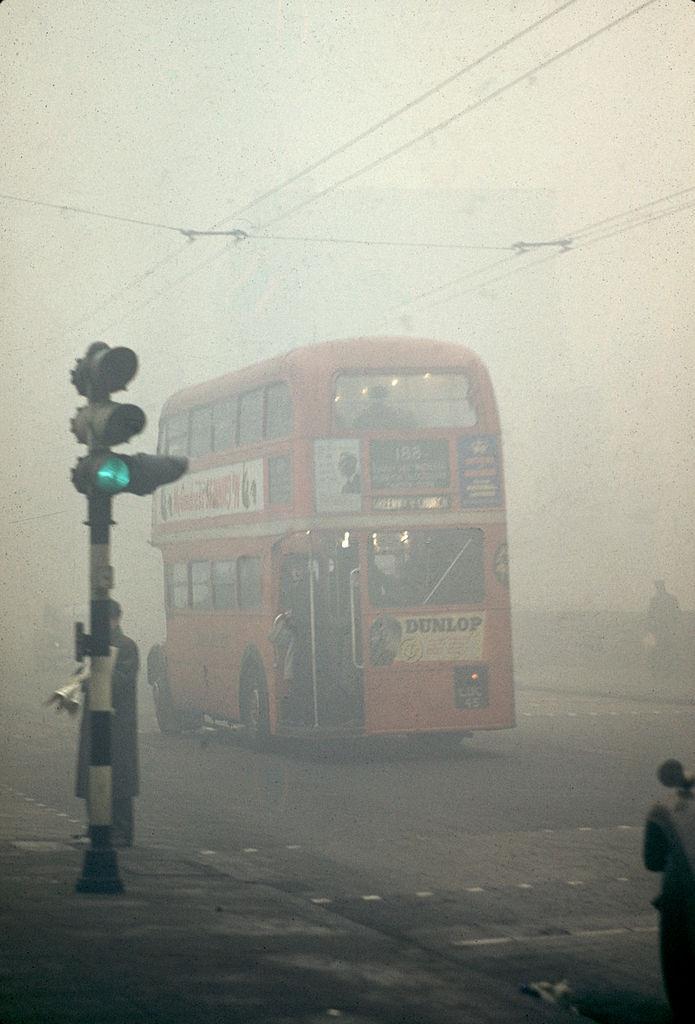 A double-decker bus drives through the fog, London, England, 1952.