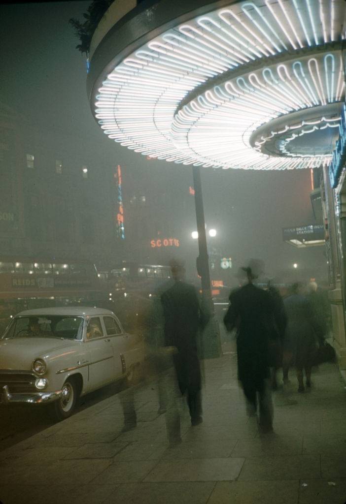 Street scene on a foggy night under the marquee of the Criterion Theatre in Piccadilly Circus, London, 1952.