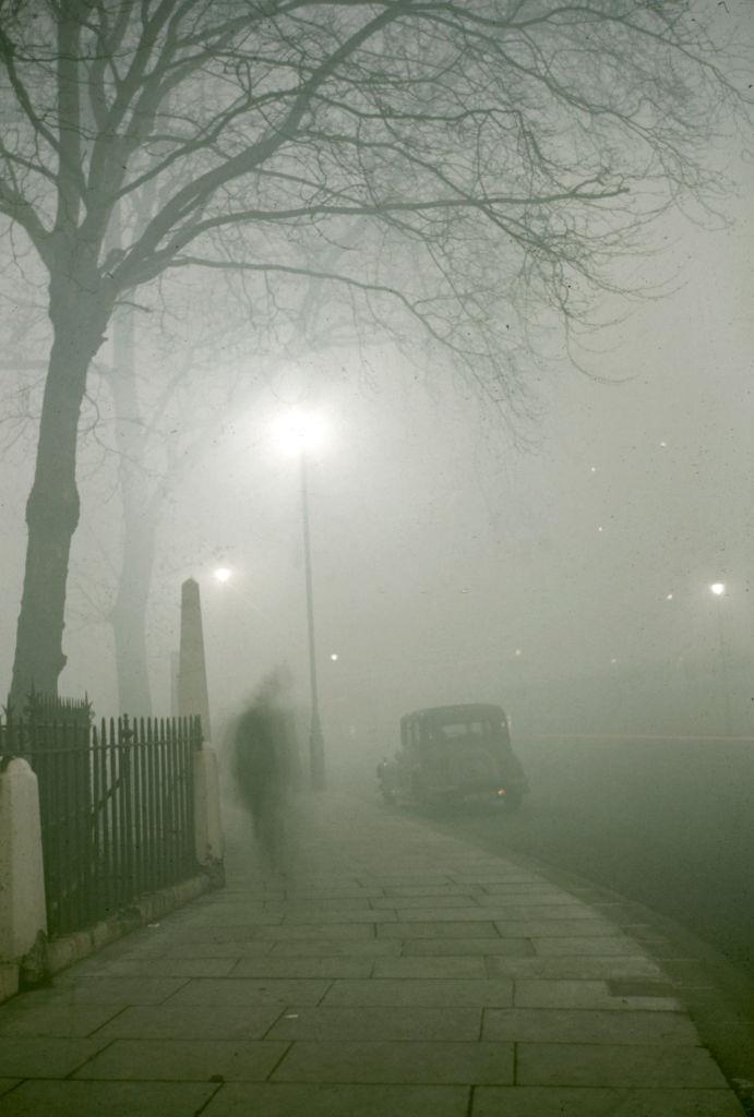View along a sidewalk in on a foggy night, London, 1952.