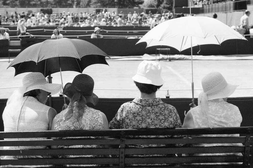 Women sitting under umbrellas for protection from harsh rays of sun during heatwave, 1976.