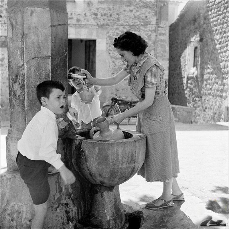 Woman removing water from a fountain with children, 1956