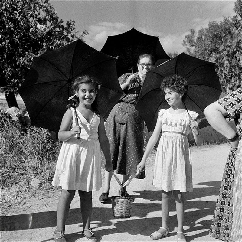 Two dolls and a woman walking with umbrellas, 1956