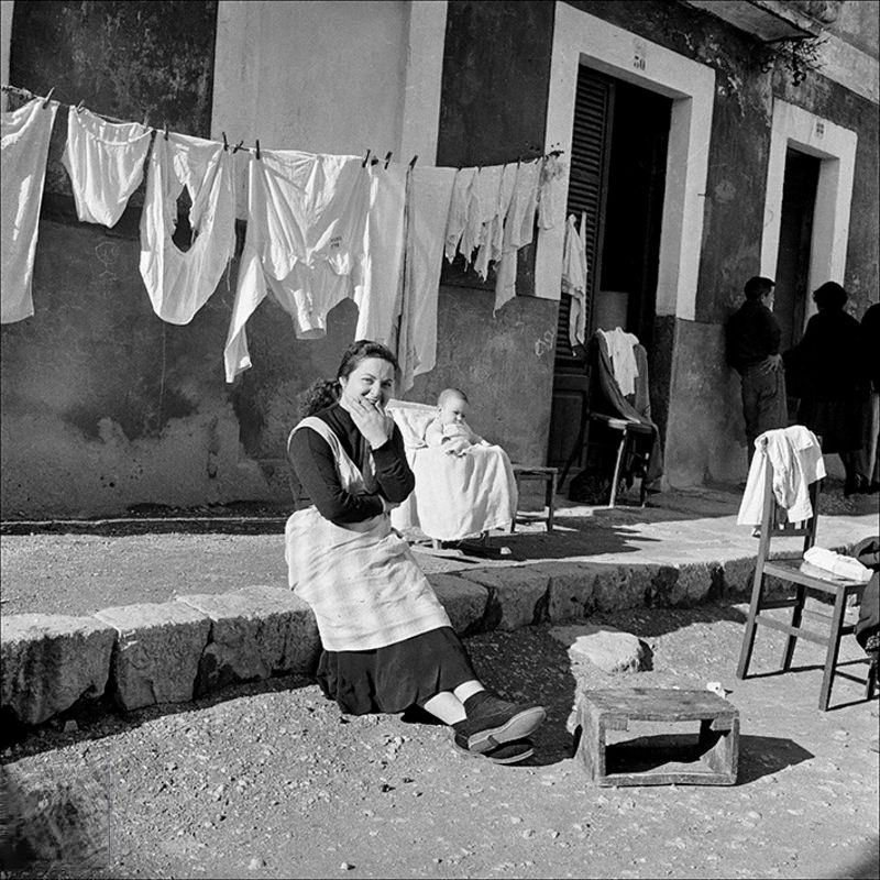 Portrait of a woman sitting with her child and clothes in the background, 1957