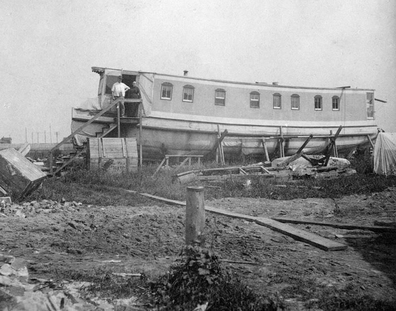 Man and woman standing at the entrance to their house, built out of the hull of a ship; an ark, circa 1900