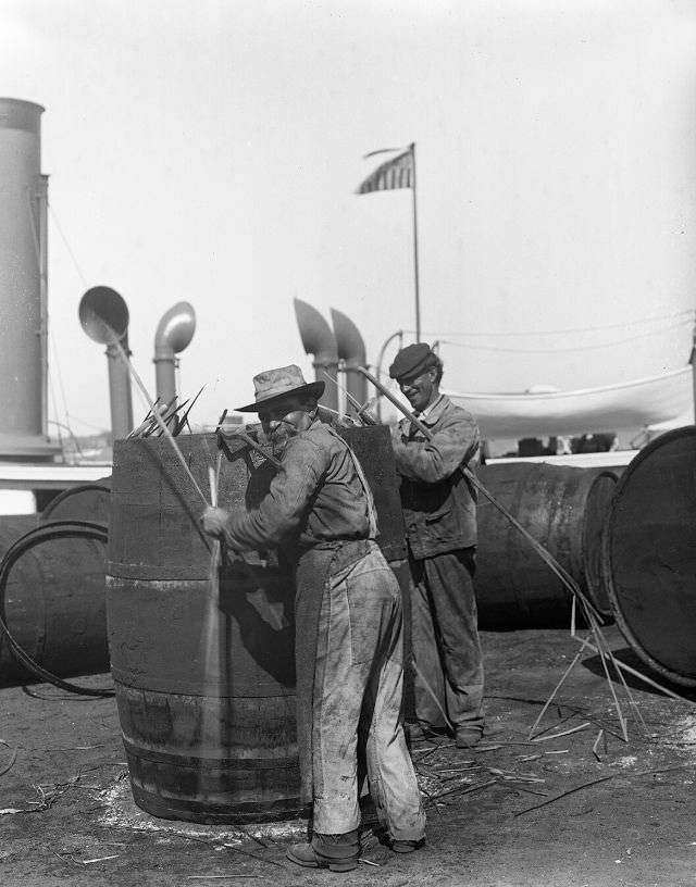 Coopers at work on oil barrels “flagging” a cask, New Bedford, 1918