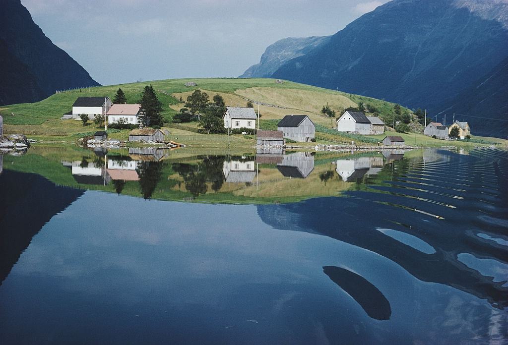 A small hamlet is reflected in the limpid waters of a Norwegian fjord, 1959.