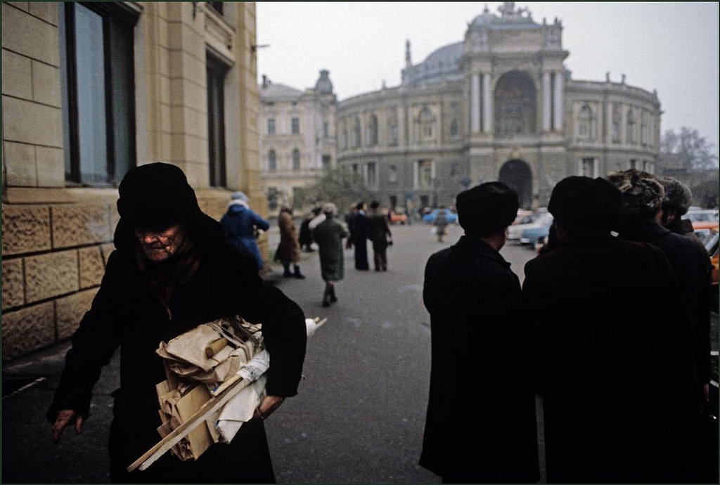 Old man with his bundle of wood and cardboard hurries along in the cold with the Opera Theatre in the background.