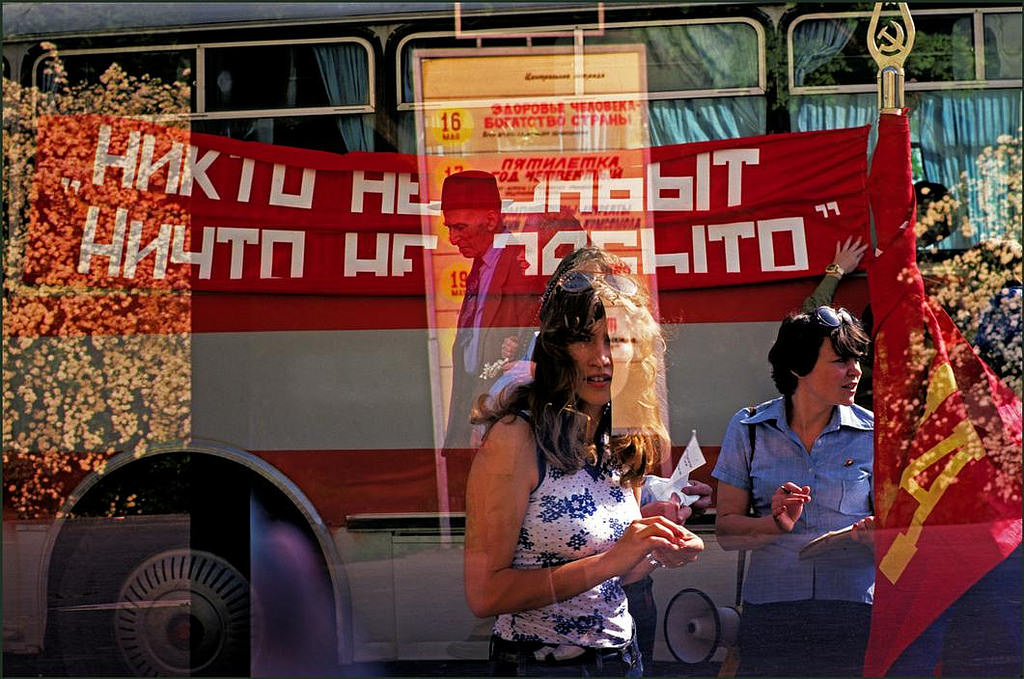 A woman looks through a cafe window whilst bus tour guide checks names.