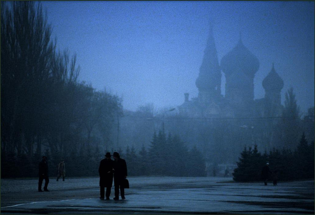 Two men confer in the early morning mist with the towers of St Panteleimon looming in the background.