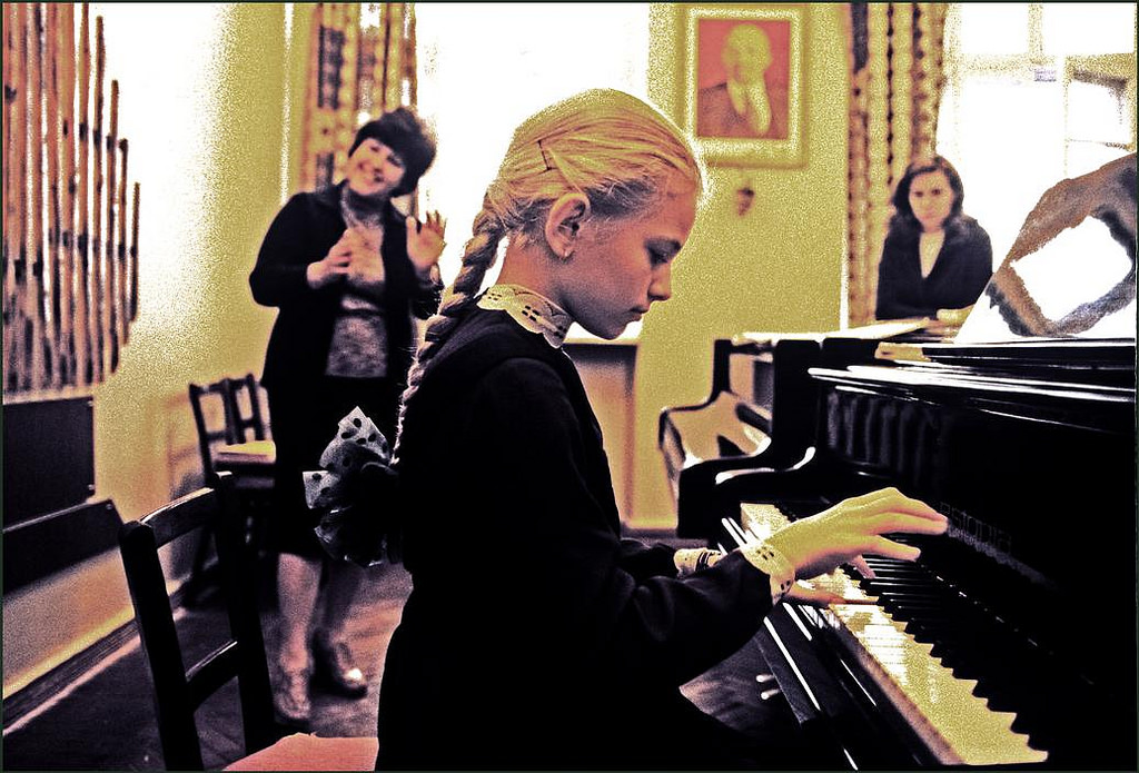 A young girl playing the piano under instruction at the famous Stolyarsky Music School with a portrait of Lenin on the wall.