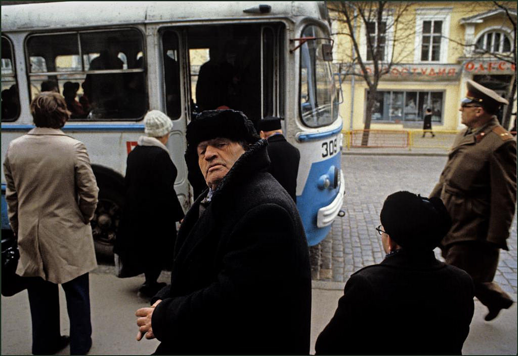 A curious man in his fur hat waiting to board a bus in the city centre.