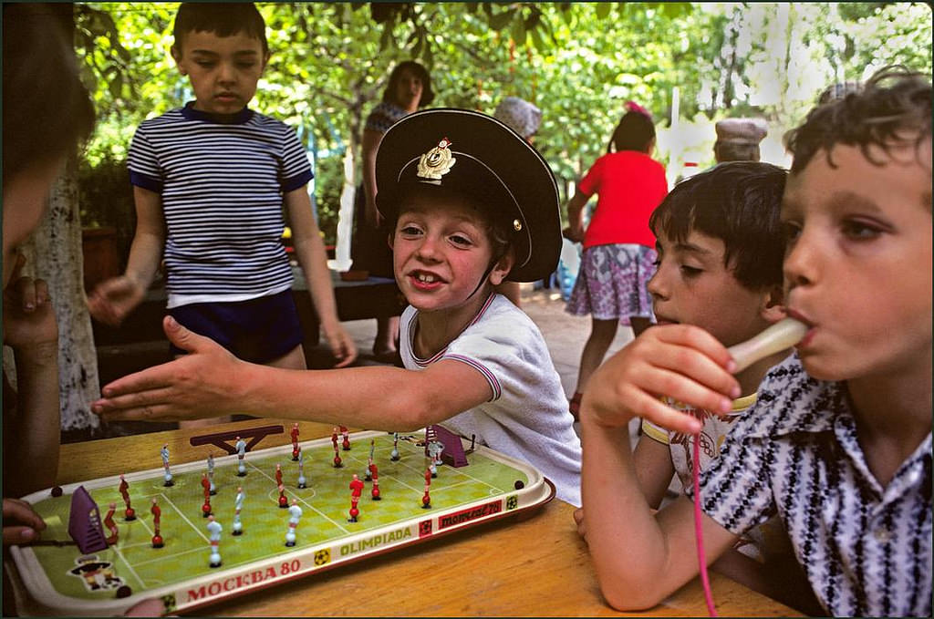 Boy in toy soldiers hat playing table football whilst another sports a black eye, in the grounds of a local kindergarten.