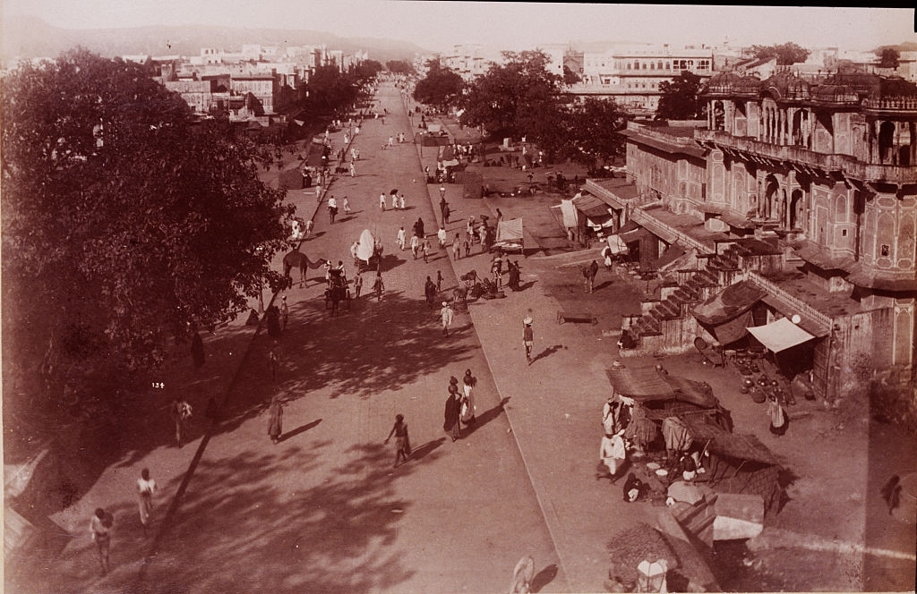 People and a camel on a wide street in a city in Ceylon, ca. 1880s.