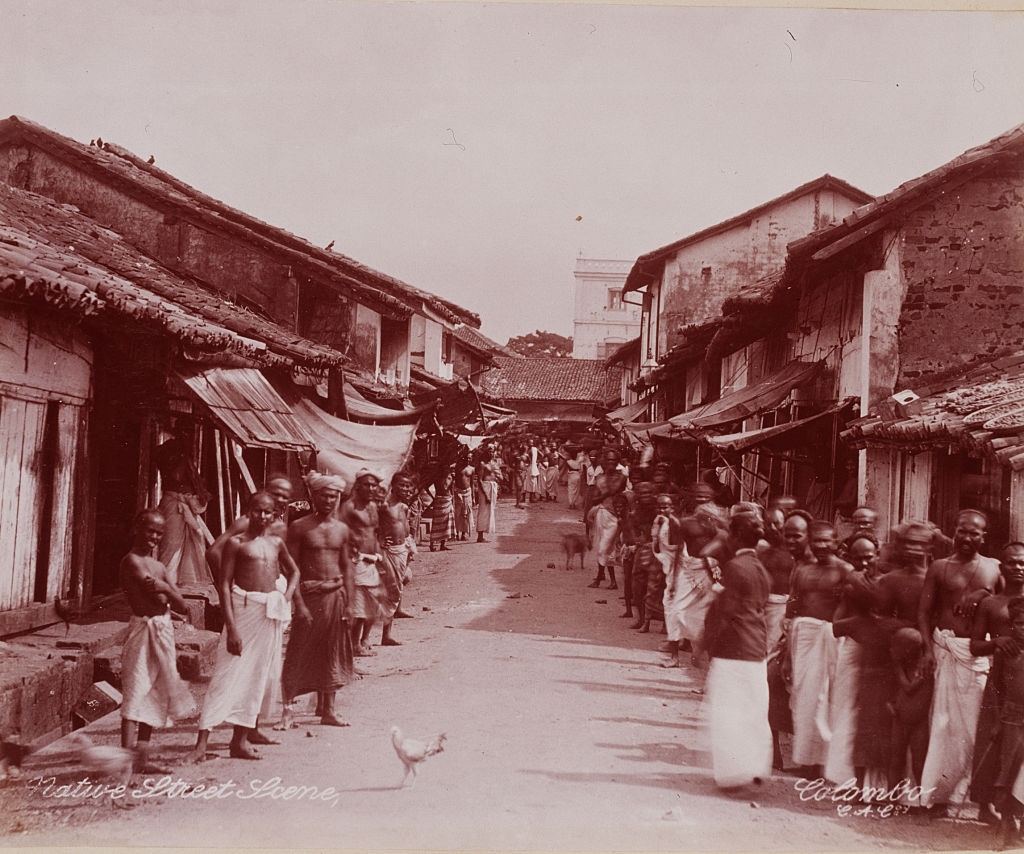 Men line a narrow street in Ceylon, 1899.