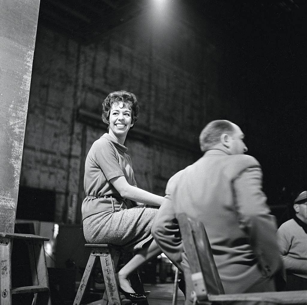 American actress and commedienne Carol Burnett sits on a stepladder backstage, along with others during the making of 'The Twilight Zone', 1962.