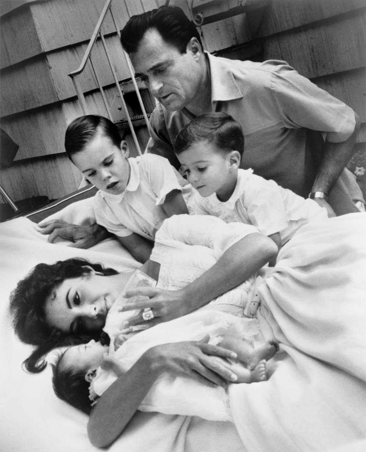 Elizabeth Taylor bottle-feeding newborn Liza Todd with her sons Christopher and Michael H. Wilding, and her husband Michael Todd observing, 1957.
