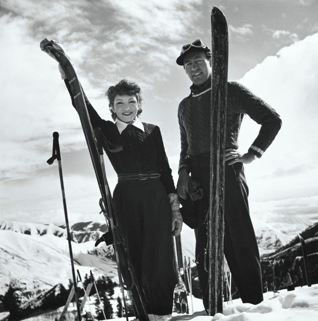 Actress Claudette Colbert and Ronald Balcom standing with skis on the slopes in Sun Valley, Idaho. Vogue 1940.