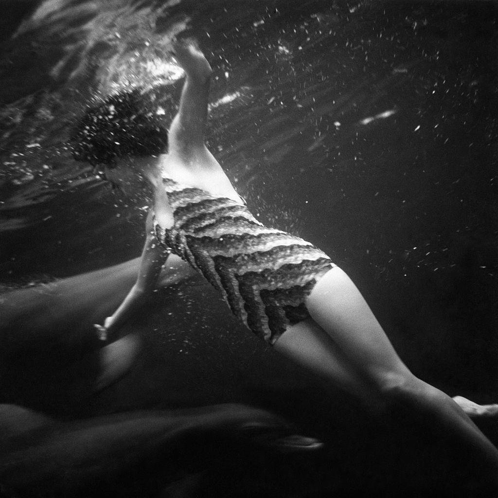 A girl swimming underwater with dolphins in a water arena, 1939.