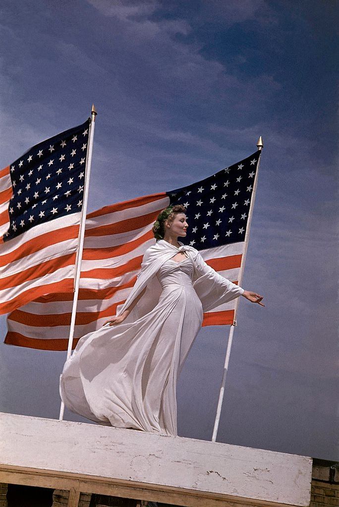 Model standing in white dress, with two American flags, 1942.