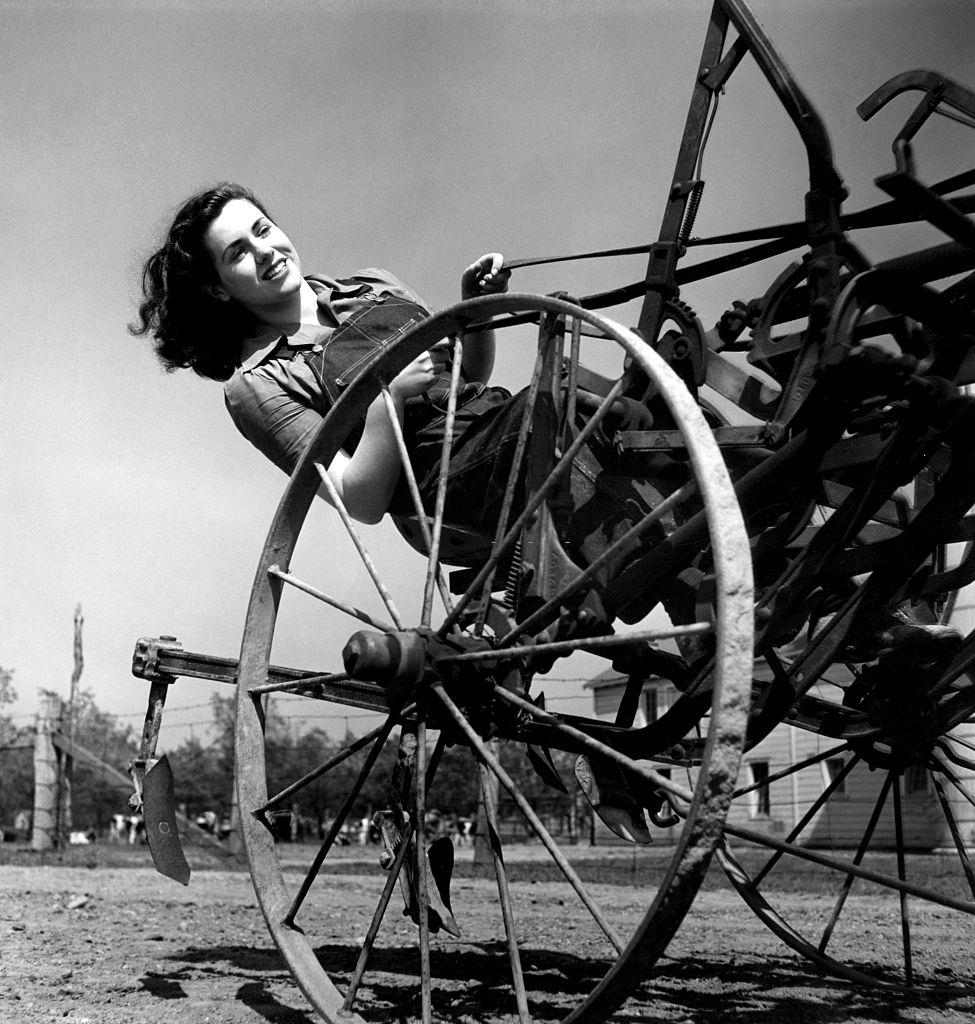 Farmer's aide, from the Women's Land Army, driving a cultivator over a field.