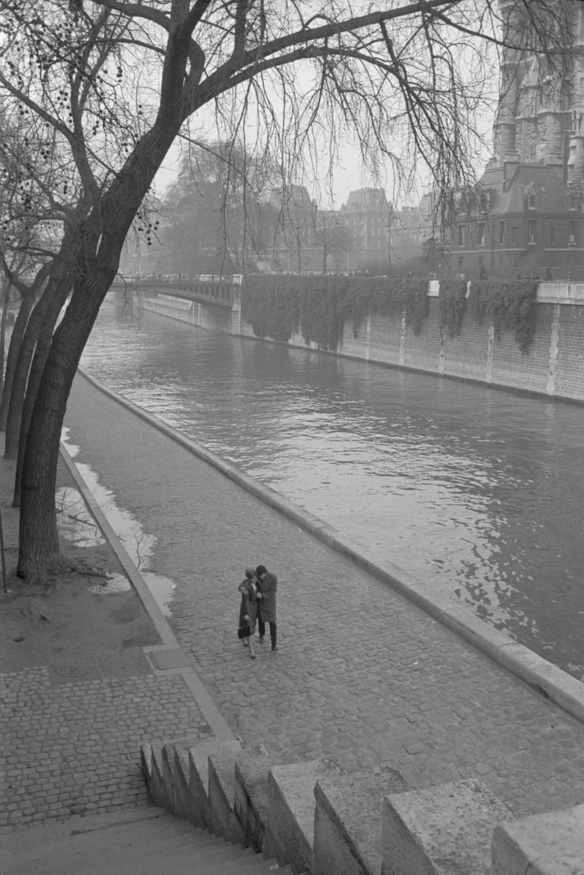A couple walking along along the Seine River.