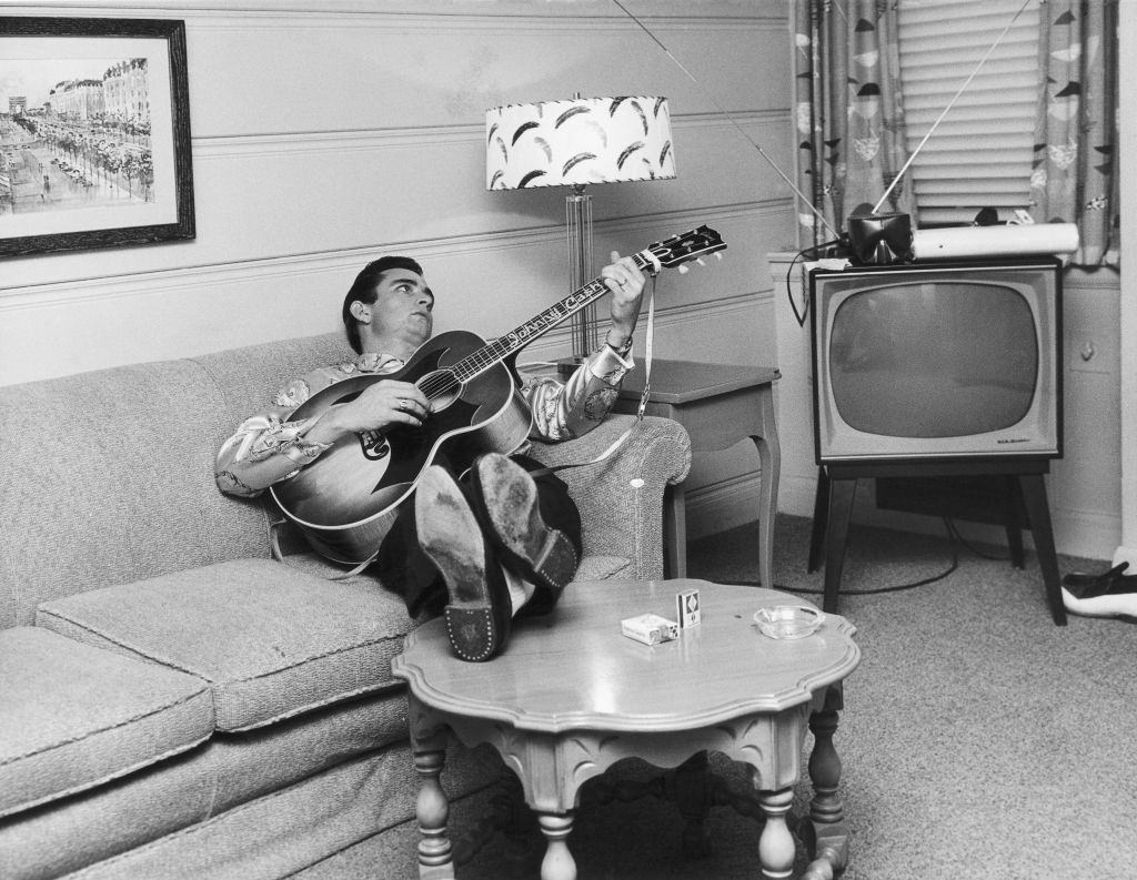 Johnny Cash reclines on a couch while playing acoustic guitar in Nashville, 1960.