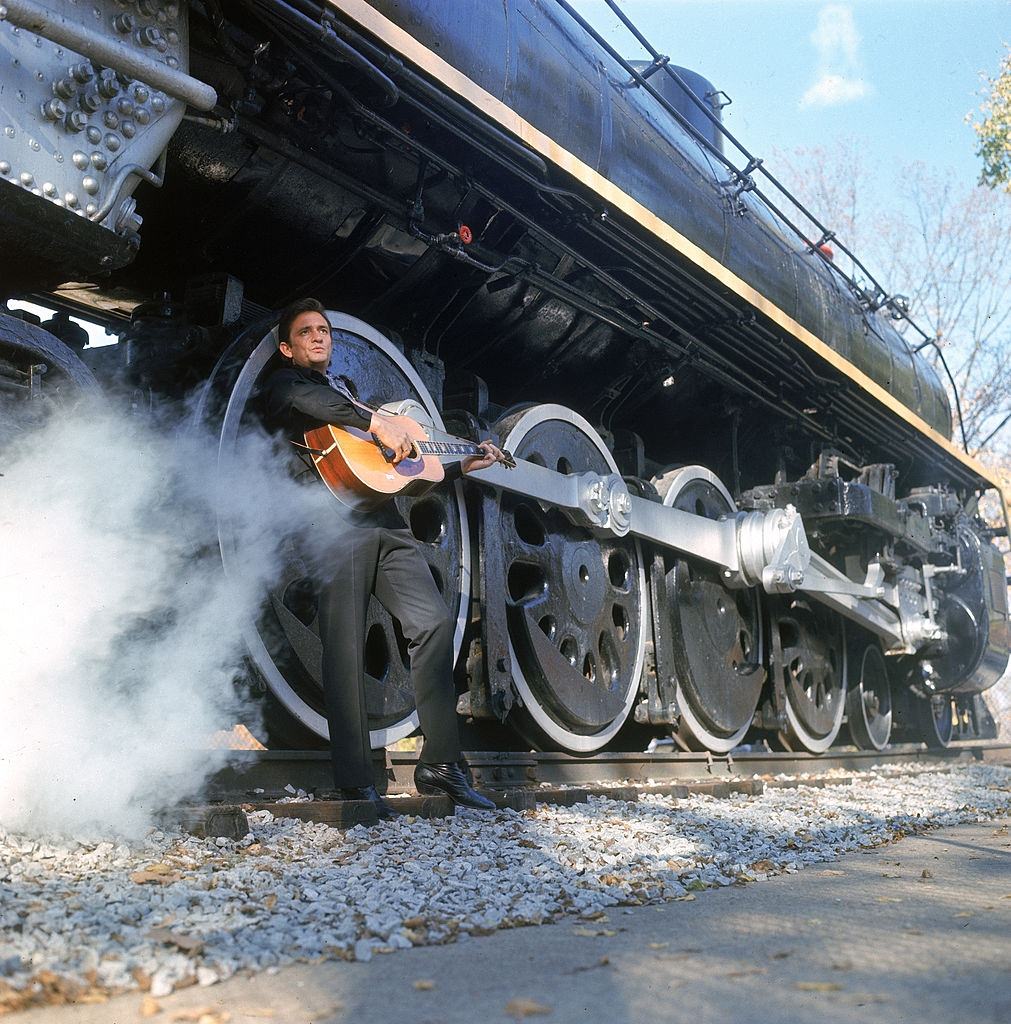 Johnny Cash with guitar by wheels of a steam train, 1969.