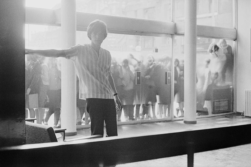 Mick Jagger waving at the fams gathered outside the studio, 1964.
