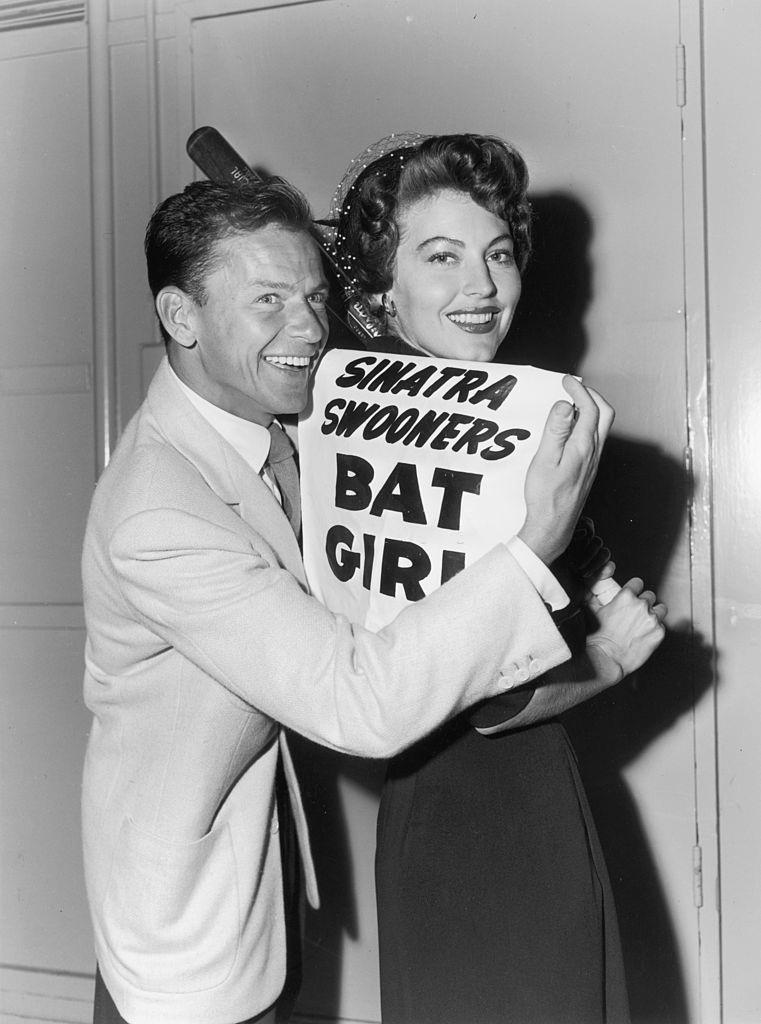 Frank Sinatra and Ava pose with a sign that reads, 'Sinatra Swooners Bat Girl,' July 12, 1949.