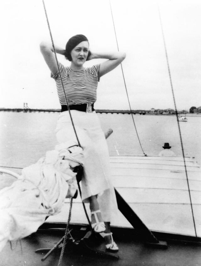 A woman is posed sitting on the boom of a sailing vessel, Queensland