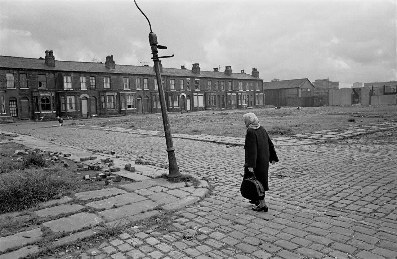 Pensioner crossing derelict land towards her home, Salford 1971
