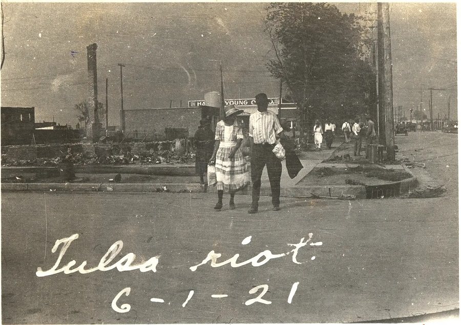 A couple walks across a street with smoke rising in the distance after the Tulsa massacre in June 1921.