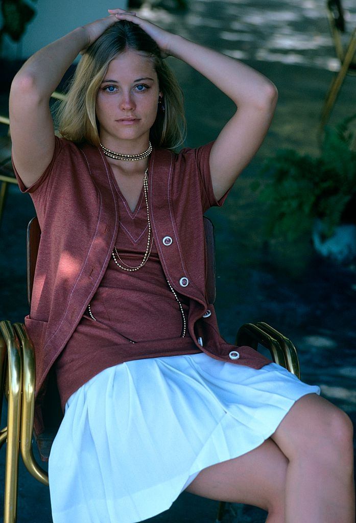 Cybill Shepherd sitting in chair wearing amber, white stitched jacket, Glamour 1970.