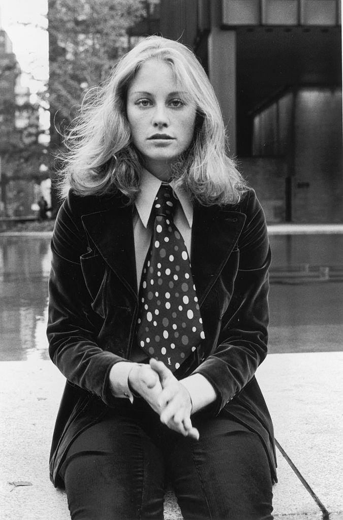 Cybill Shepherd sitting on a concrete wall in front of a fountain, 1971.