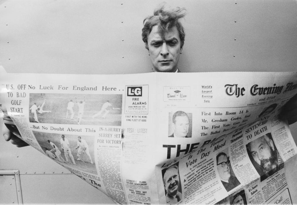 Michael Caine reading a copy of the Evening News, 1960s.