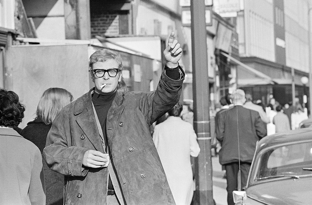 Michael Caine waving towards the taxi in London, 1965.