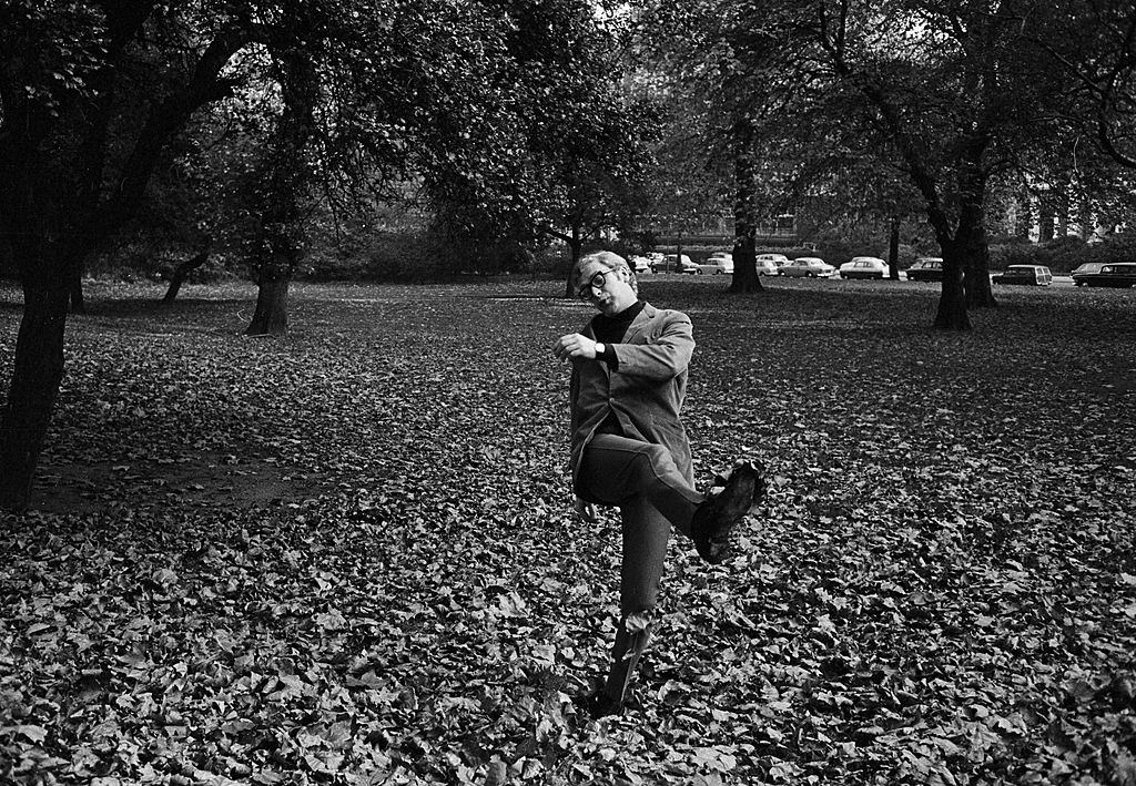 Michael Caine kicks, in a London park covered with fallen leaves, 1965.
