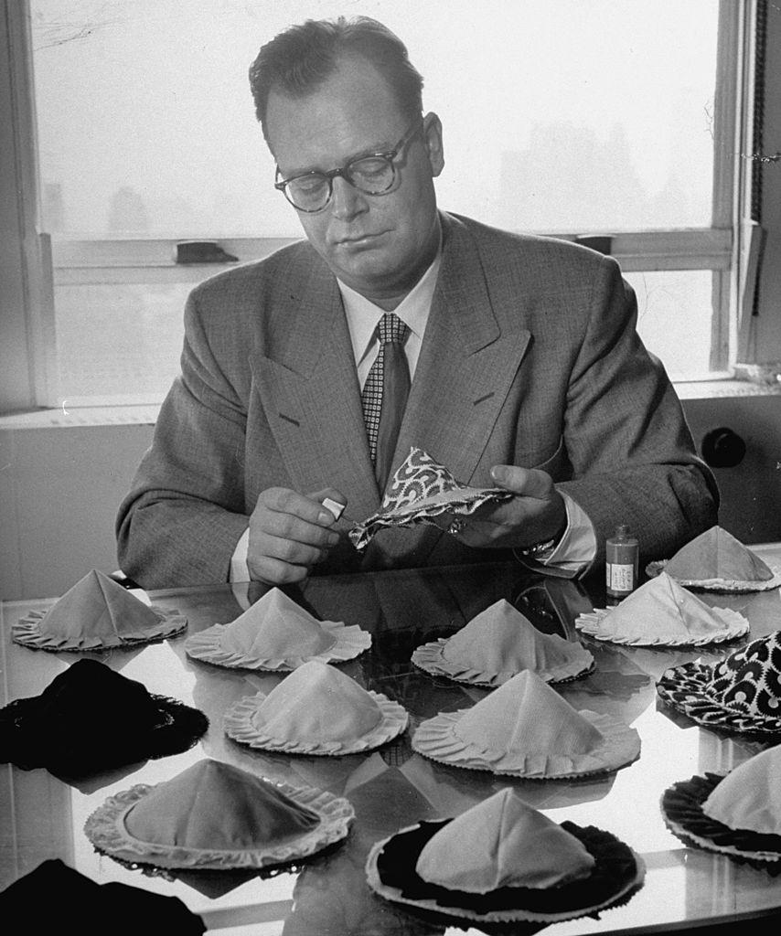 Inventor of Poses, Charles L. Langs sitting at his desk full of his inventions, strapless, backless, wireless bras.